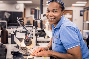 A seamstress smiles while sewing automotive leather seat covers. 
