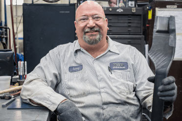 A sheet metal worker holds a part and smiles for the camera. 