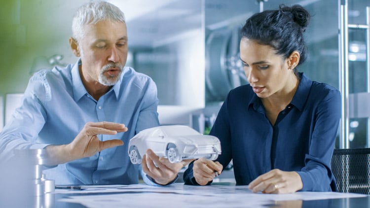 Man and woman hold low volume production car model in hands while looking at diagram